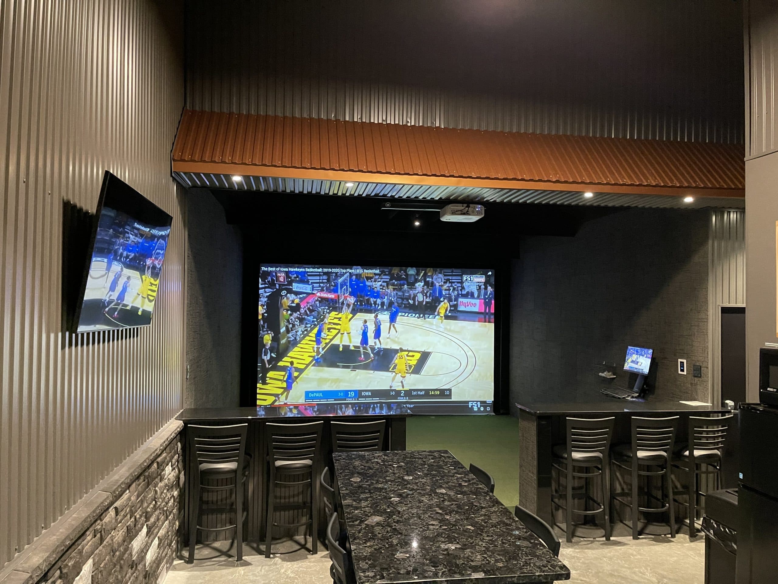 Double suite with a wall-mounted TV, granite bar and simulator screen streaming a basketball game